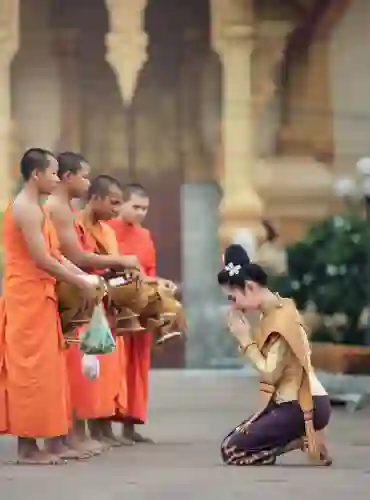 Jeune femme en tenue traditionnelle offrant des aumônes à des moines bouddhistes en Thaïlande.