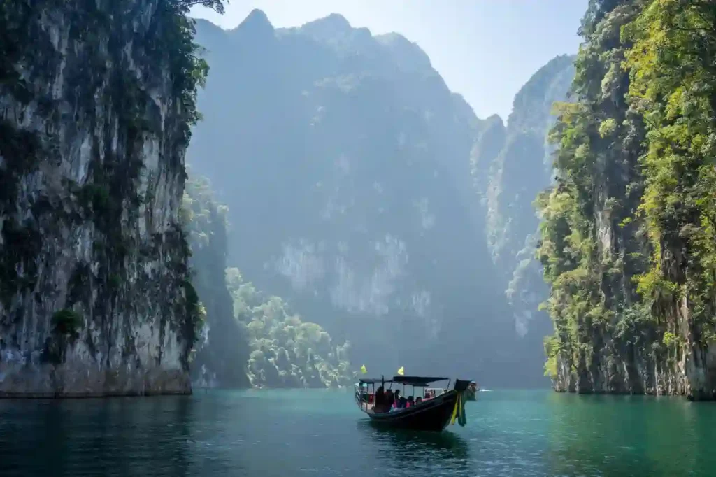 Bateau traditionnel naviguant sur un lac turquoise entouré de falaises karstiques et de jungle luxuriante en Thaïlande, illustrant la sérénité et la sécurité de la destination